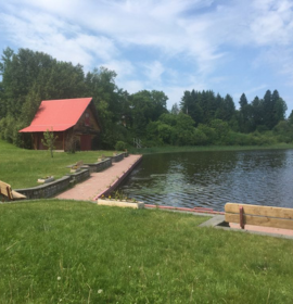 Timmins Care A serene lakeside in Timmins, with a red-roofed cabin and a small wooden dock under a blue sky with scattered clouds. Cochrane District Social Services Administration Board